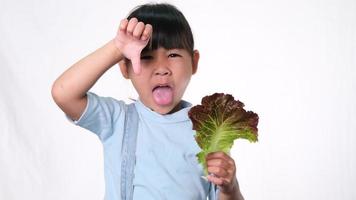 petite fille heureuse avec salade fraîche avec montrant les pouces vers le haut sur fond blanc en studio. bonne habitude saine pour les enfants. concept de soins de santé video