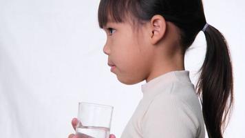 menina asiática bonitinha bebendo água de um copo no fundo branco no estúdio. bom hábito saudável para as crianças. conceito de saúde video
