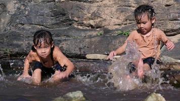 Asiatisches kleines Mädchen, das mit ihrer Schwester im Waldbach spielt. aktive erholung mit kindern am fluss im sommer. video