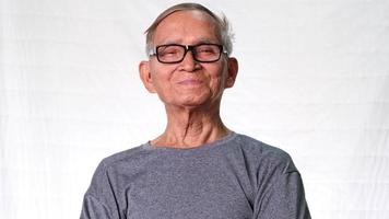 Aziatische senior man lacht gelukkig thuis. vrolijke oude man genoot van zijn pensioen en keek binnenshuis naar de camera. video