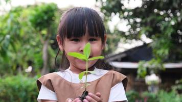 jolie petite fille tenant un petit arbre dans sa main sur un fond vert flou au printemps. concept d'écologie du jour de la terre video