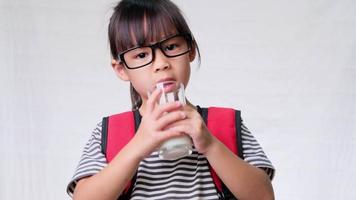 linda colegial bebendo leite de um copo antes de ir para a escola. alimentação saudável para crianças. de volta ao conceito de escola video