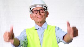 Happy senior engineering architect wearing a vest and helmet shows thumbs up on a white background in studio. video