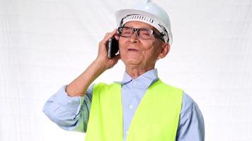 costruttore di architetto senior di ingegneria che indossa giubbotto di sicurezza e casco per discutere di lavoro al telefono su sfondo bianco in studio. video