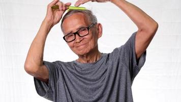 Elderly man combing hair with green comb on white background in studio.