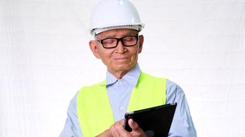 Senior architect engineering builder wearing safety vest and helmet looks at work on digital tablet on white background in studio. video