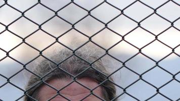 Desperate Senior Man Looking To The Sky Through Metal Wire Mesh. video