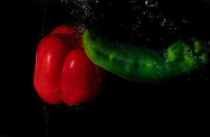 red and green bell pepper in water with splash on black background. photo