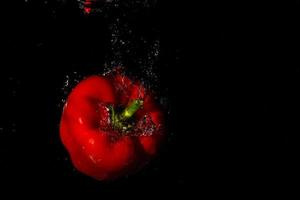 red bell pepper in water with splash on black background. photo