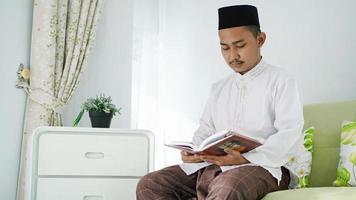 retrato de un musulmán asiático sentado en un sofá leyendo el Corán en casa