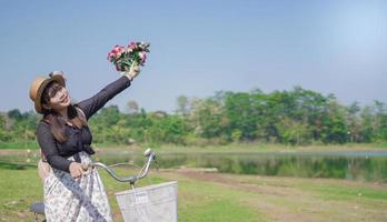 joven asiática disfrutando del ciclismo sosteniendo flores en el parque