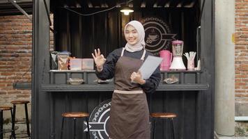 hermosa camarera asiática trae la lista del menú haciendo un gesto de ok en el contenedor de la cabina del café foto