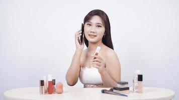 Hermosa discusión de maquillaje asiático en el teléfono aislado sobre fondo blanco. foto