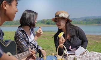 Group of young women and men sitting, eating and playing guitar in the park in spring summer photo