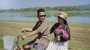 feliz joven pareja asiática en bicicleta sosteniendo flores en verano foto