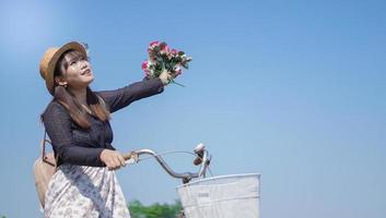 joven asiática disfrutando del ciclismo sosteniendo flores en el parque foto