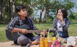 young asian couple laughing and playing guitar on vacation in park photo