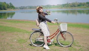 young asian woman enjoying cycling holding flowers in park photo