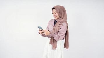 Hermosa mujer en hijab jugando smartphone disfrutando aislado sobre fondo blanco. foto