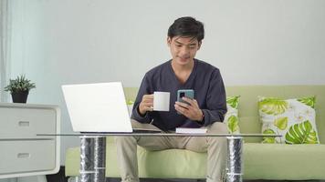 asian man playing smartphone while enjoying a drink at home photo