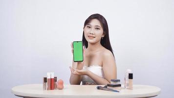 hermoso maquillaje asiático que muestra la pantalla del teléfono inteligente aislada en el fondo blanco foto
