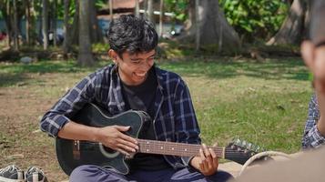 asian young man playing guitar on vacation in park photo