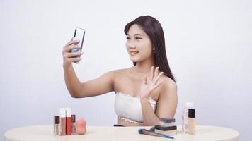 Hermoso maquillaje asiático saluda smartphone aislado sobre fondo blanco. foto