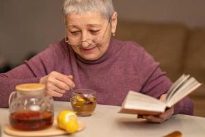 woman sitting at the table drinking tea with lemon and reading a book photo