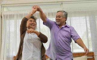 Spending time together at home, an elderly Asian couple having fun dancing in the living room. photo