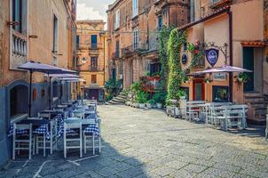 tropea, italia - 8 de mayo de 2018 típica calle estrecha italiana del centro histórico de la ciudad de tropea con edificios antiguos y restaurante callejero