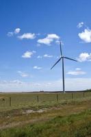 a power generating wind turbine sits in a field under a blue sky photo