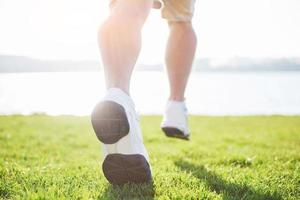 Outdoor cross-country running in summer sunshine concept for exercising, fitness and healthy lifestyle. Close up of feet of a man running in grass photo