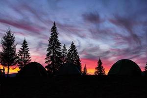 Majestic sky, pink cloud against the silhouettes of pine trees in the twilight time, tents on the front. Carpathians, Ukraine, Europe. Discover the world of beauty photo