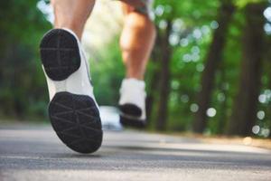 Outdoor cross-country running in concept for exercising, fitness and healthy lifestyle. Close up of feet of young runner man running along road in the park photo