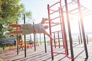 Muscular man with beautiful torso exercising on horizontal bars on a blurred park background. Young man doing pull-ups outdoors photo