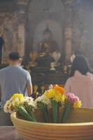 un par de personas rezan a buda en el templo religioso tradicional de tailandia. ramo floral en primer plano. hermosa cultura budista respeto estilo de vida. feliz familia novia y novio. foto