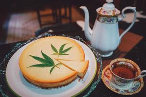 Cheesecake dessert pie, dairy recipe homemade on table. Delicious fresh peace of cake slice on plate. Tasty sweet food cannabis leaves on top. Morning gourmet plate closeup dish photography. photo