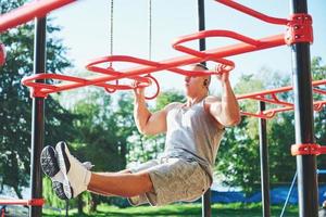 Muscular man with beautiful torso exercising on horizontal bars on a blurred park background. Young man doing pull-ups outdoors photo