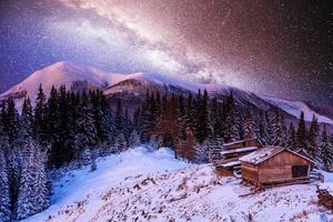 magical winter snow covered trees and mountain village. Winter landscape. Vibrant night sky with stars and nebula and galaxy. photo