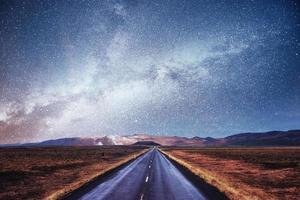 Starry Sky over the mountains. The asphalt road with white markings. Beautiful summer landscape. Soft filtering effect. Iceland photo
