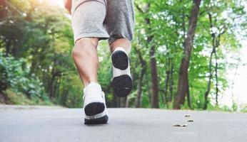 Outdoor cross-country running in concept for exercising, fitness and healthy lifestyle. Close up of feet of young runner man running along road in the park photo