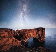 Cape Dyrholaey at southern Iceland. Altitude 120 m, and mean hill island with a door opening. Vibrant night sky with stars and nebula and galaxy. Deep sky astrophoto photo