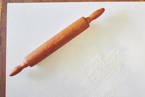 Wooden rolling pin with white wheat flour on the table. top view photo
