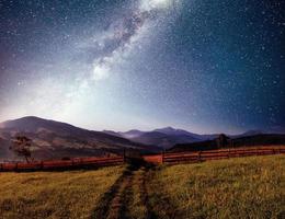 Mountain summer landscape. High grass and vibrant night sky with stars and nebula and galaxy. Deep sky astrophoto