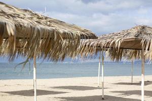 playa exótica en la playa con sombrilla. una sombrilla de playa vacía y solitaria hecha de juncos. hermosas ramas secas de palmeras en el techo con el telón de fondo de la playa. foto