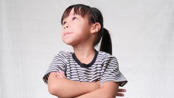 Cute little girl looking up with her arms crossed and thinking something on white studio background. concept of imagination video