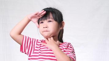 Cute little girl holding hand at forehead, looking far away distance on white background in studio. video