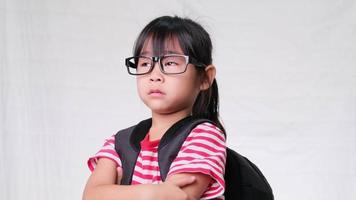 Cute schoolgirl wearing glasses with backpack, looking up, thinking of something fun and having an idea, concept of imagination. video