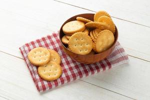 Rounded cracker cookies in a wooden bowl with tablecloth on white wooden table background photo