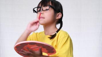 Cute little girl holding a brush painting an imaginary picture on white background in studio. concept of education and imagination video